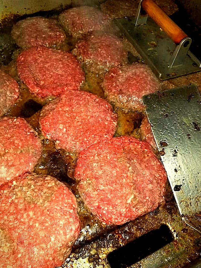 Hand-pattied burger patties sizzling on Tony's flat-top grill